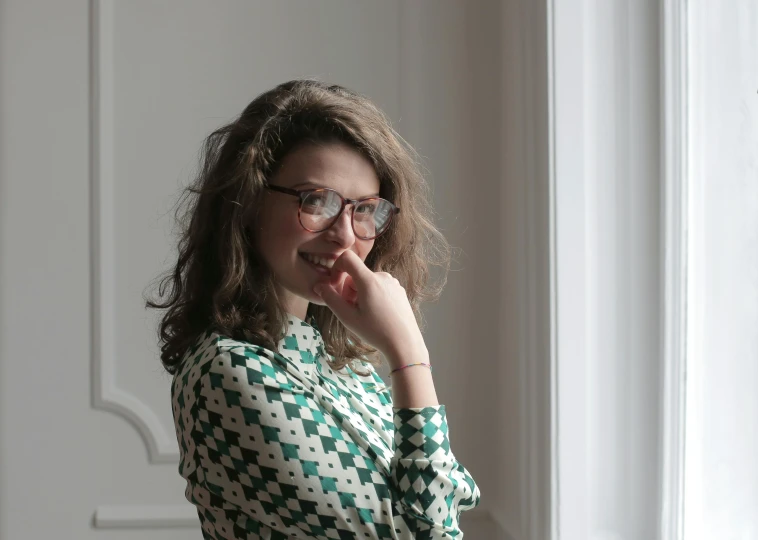 a woman standing in front of a window talking on a cell phone, by Emma Andijewska, pexels contest winner, op art, square rimmed glasses, girl with brown hair, delicate patterned, lovingly looking at camera