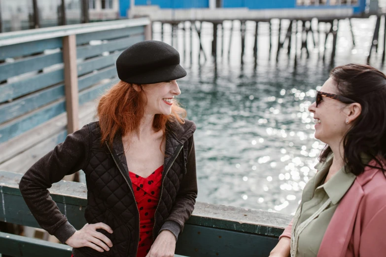 two women sitting on a bench next to a body of water, a portrait, by Winona Nelson, pexels, happening, wearing a french beret, near a jetty, ( redhead, harbour