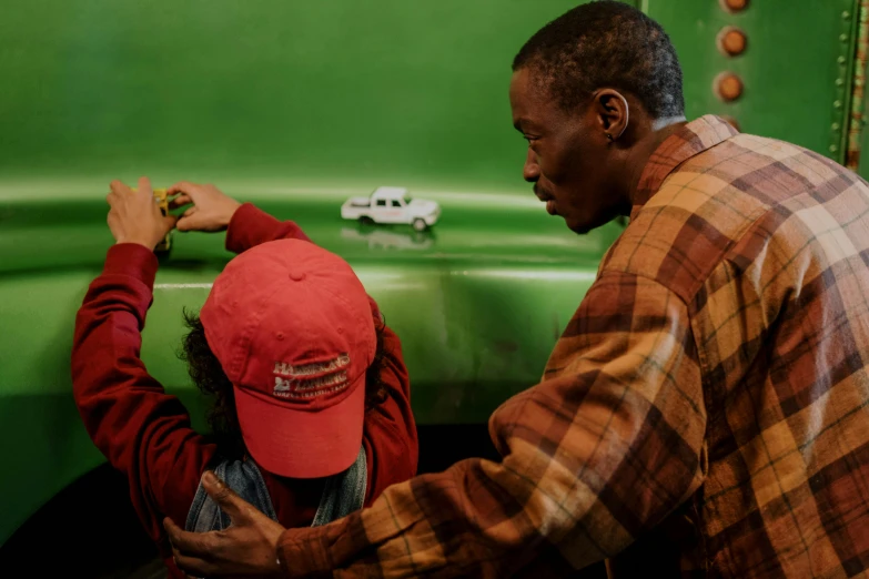 a man standing next to a little girl in front of a green truck, by Nathalie Rattner, pexels contest winner, with eddie murphy, in a workshop, movie scene close up, ignant