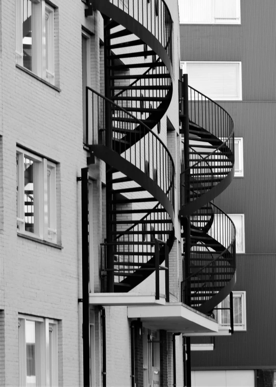 a black and white photo of a building with a spiral staircase, precisionism, high contrast colours, footbridges between houses, outdoor staircase, dna helix