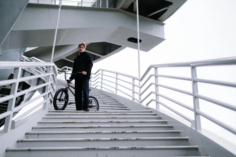 a man standing on a set of stairs next to a bicycle, felix englund style, overpass, mr beast, portait image