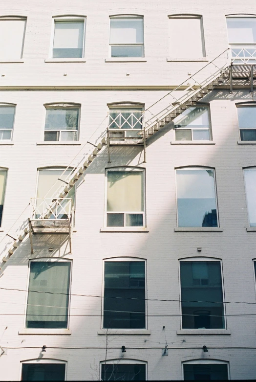 a fire escape ladder on the side of a building, inspired by Elsa Bleda, unsplash, postminimalism, low quality photo, montreal, white houses, 2000s photo