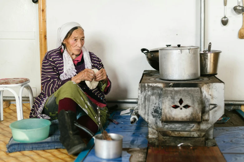 a woman sitting on the floor in front of a stove, by Julia Pishtar, pexels contest winner, cloisonnism, mongolia, breakfast, thumbnail, settlement