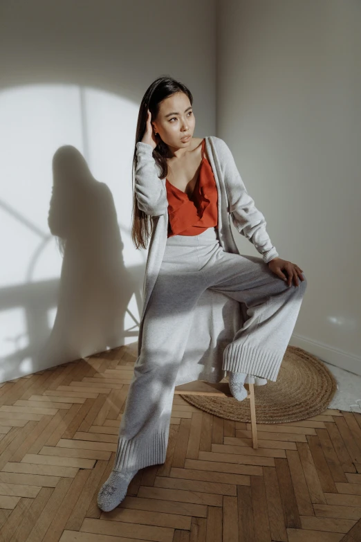 a woman sitting on a chair in a room, inspired by Ruth Jên, trending on pexels, photorealism, large pants, wearing in cardigan, soft grey and red natural light, young asian woman