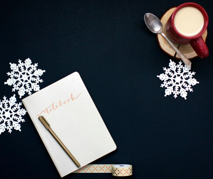 a notepad sitting on top of a table next to a cup of coffee, snowflakes, ivory and copper, notebook, navy