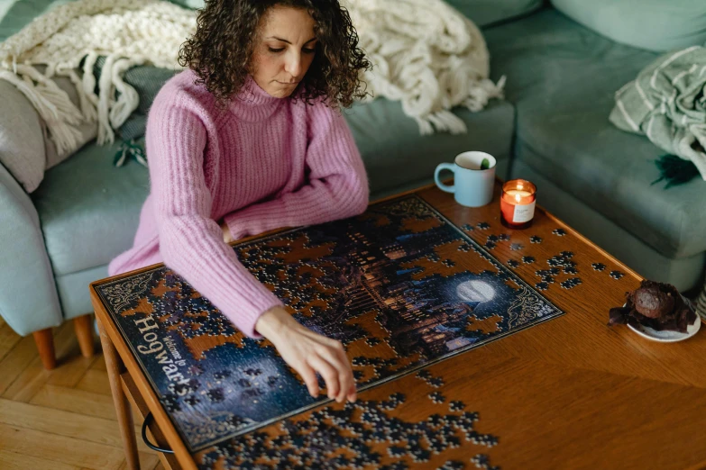 a woman sitting at a table with a puzzle, a jigsaw puzzle, by Julia Pishtar, hogwarts setting, cosy enchanted scene, midnight, wooden coffee table