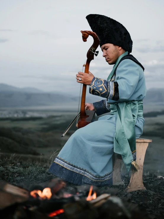 a woman sitting on top of a wooden bench next to a fire, an album cover, inspired by Konstantin Vasilyev, pexels contest winner, hurufiyya, man holding spear, ferred - themed robes and hat, song nan li, performing