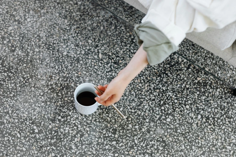 a person sitting on a couch holding a cup of coffee, inspired by Louis Stettner, unsplash, minimalism, on the concrete ground, holding a thick staff, enamel, all marble