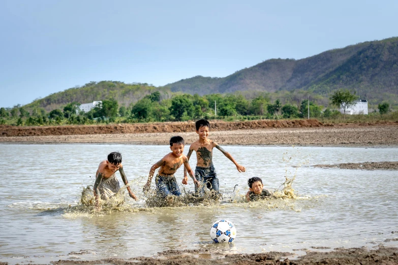 a group of children playing in the water with a soccer ball, inspired by Steve McCurry, unsplash contest winner, on a soccer field, 15081959 21121991 01012000 4k, brown mud, in style of thawan duchanee