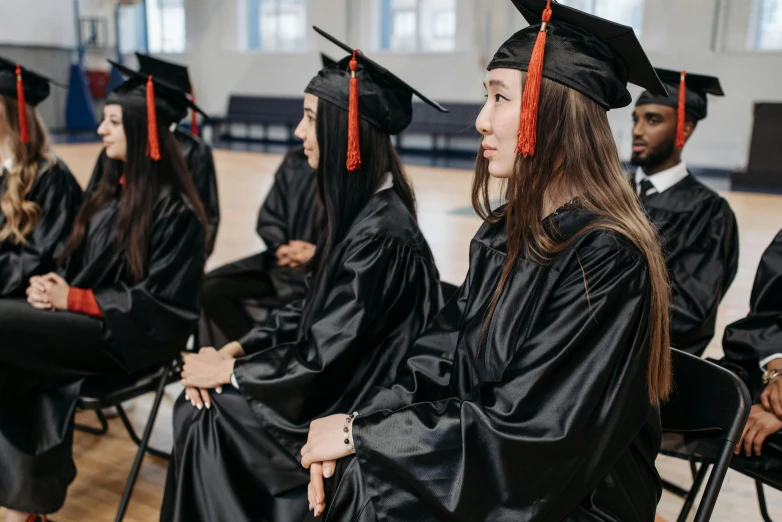 a group of graduates sitting in chairs in a gym, shutterstock, academic art, black pointed hat, asian women, 🦩🪐🐞👩🏻🦳, wearing a velvet robe