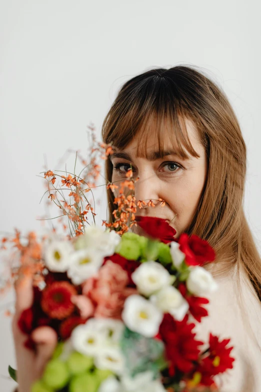 a woman holding a bouquet of flowers in front of her face, brown hair and large eyes, red brown and white color scheme, looking off to the side, zoomed in