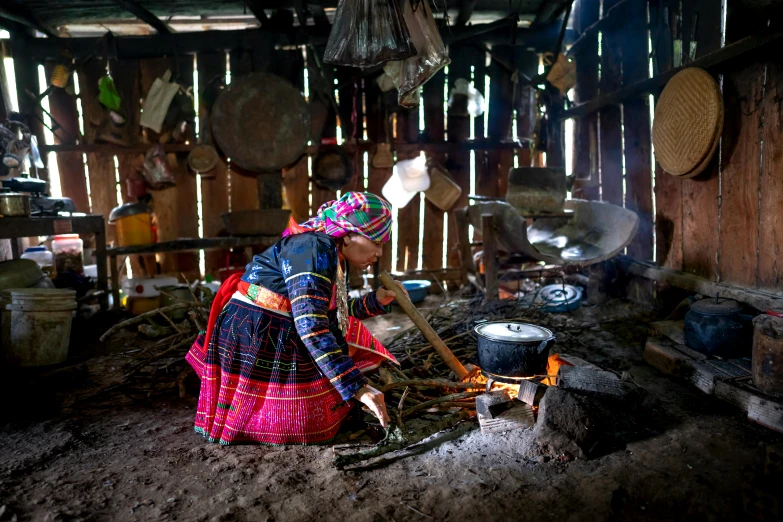 a woman cooking over an open fire in a hut, by Julia Pishtar, pexels contest winner, shipibo patterns, wearing traditional garb, then another, press