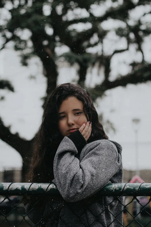 a woman standing in front of a fence talking on a cell phone, trending on pexels, realism, pretty girl standing in the rain, resting head on hands, wearing a turtleneck and jacket, curls