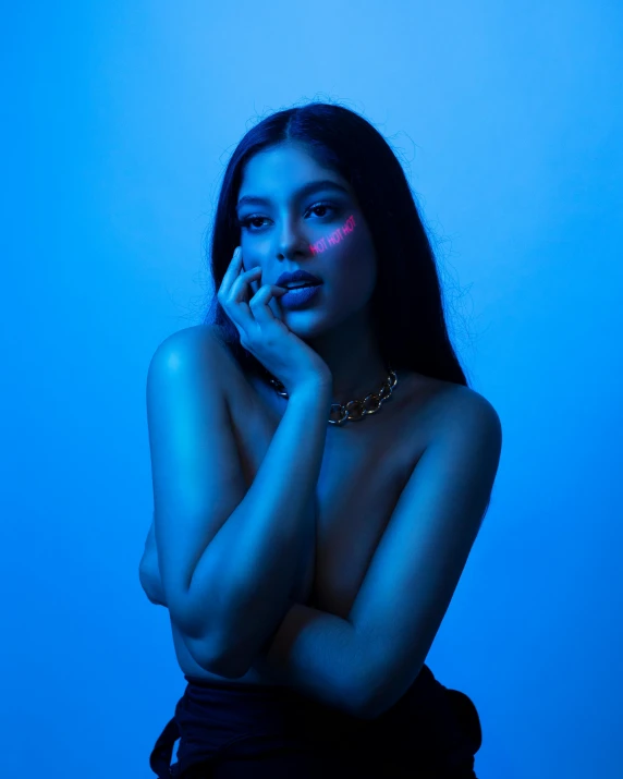 a woman sitting on a stool talking on a cell phone, an album cover, inspired by Elsa Bleda, trending on pexels, holography, blue body paint, portrait of zendaya, blue and red lights, provocative indian
