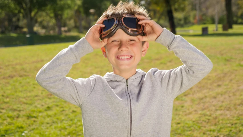 a young boy holding a pair of sunglasses over his head, by David Simpson, pexels, wearing human air force jumpsuit, avatar image, happy sunny day, wearing goggles