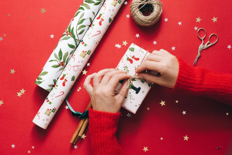 a person wrapping christmas presents with twine of twine of twine of twine of twine of twine of twine of twin, a picture, by Julia Pishtar, emma bridgewater and paperchase, on a red background, the warm, canva