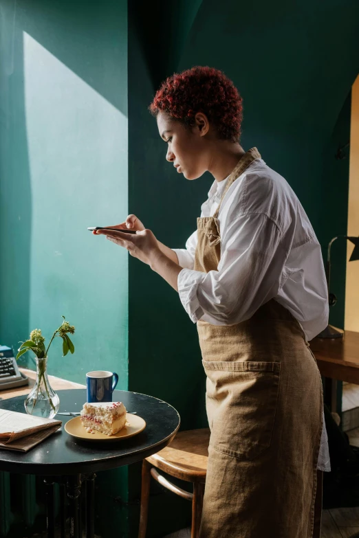 a woman standing at a table in front of a laptop, trending on pexels, renaissance, culinary art photography, looking at his phone, copper and deep teal mood, white apron