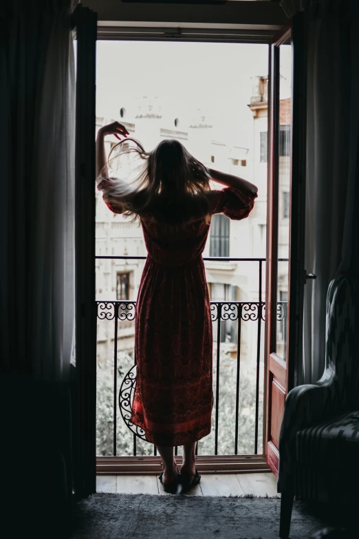 a woman in a red dress standing in front of a window, inspired by Elsa Bleda, pexels contest winner, arabesque, waking up, balcony door, her hair is tied above her head, instagram post