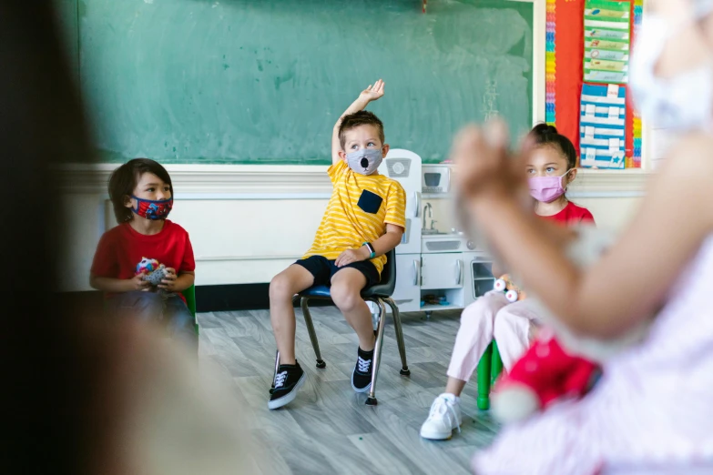 a group of children sitting in front of a blackboard, by Drew Tucker, pexels, surgical mask covering mouth, holding his hands up to his face, zachary corzine, pictured from the shoulders up