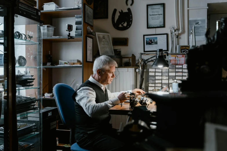 a man sitting at a desk working on a typewriter, a portrait, by Jakob Gauermann, pexels contest winner, professional gunsmithing, silver jewellery, hasselblad quality, portrait of an old