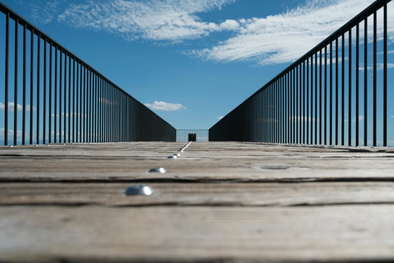 a wooden bridge over a body of water, an album cover, inspired by Storm Thorgerson, unsplash, minimalism, blue sky, street perspective, ( ( railings ) ), eyelevel perspective image