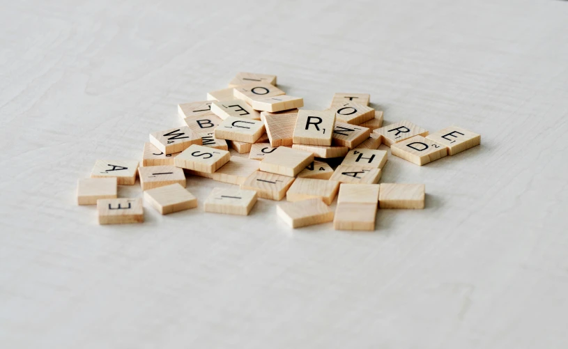 a pile of scrabbles sitting on top of a table, by Emma Andijewska, unsplash, letterism, on a pale background, gif, a wooden, tan