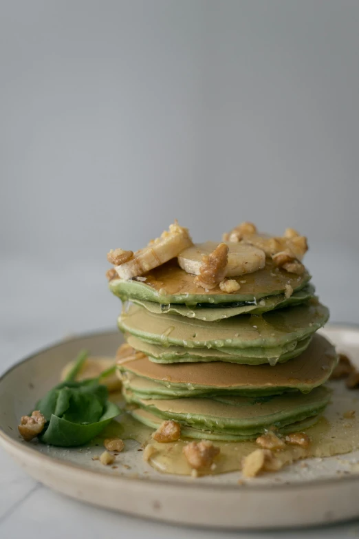 a stack of pancakes sitting on top of a white plate, inspired by Kanō Tan'yū, unsplash, moringa juice, metalic green, nut, birch