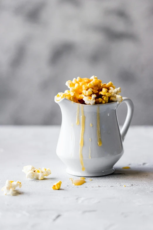 a cup filled with popcorn sitting on top of a table, melted cheddar, dramatic product shot, square, drippy