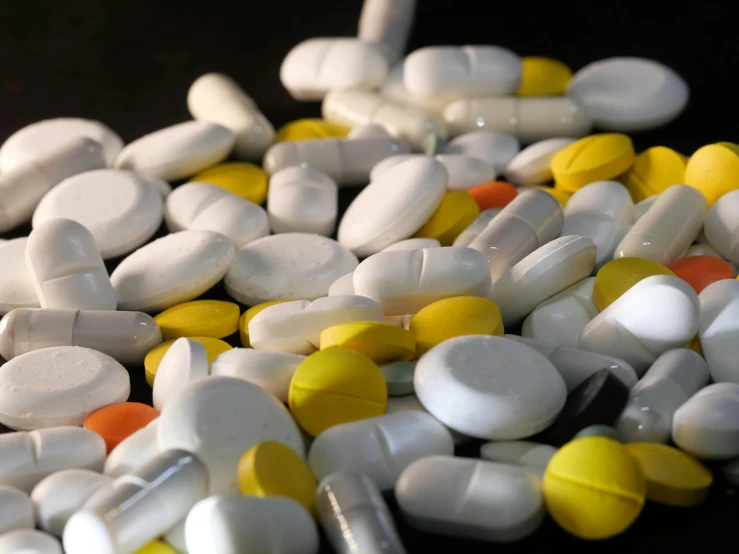 a pile of pills sitting on top of a table, antipodeans, with a black background, varying ethnicities, white and yellow scheme, sterile colours