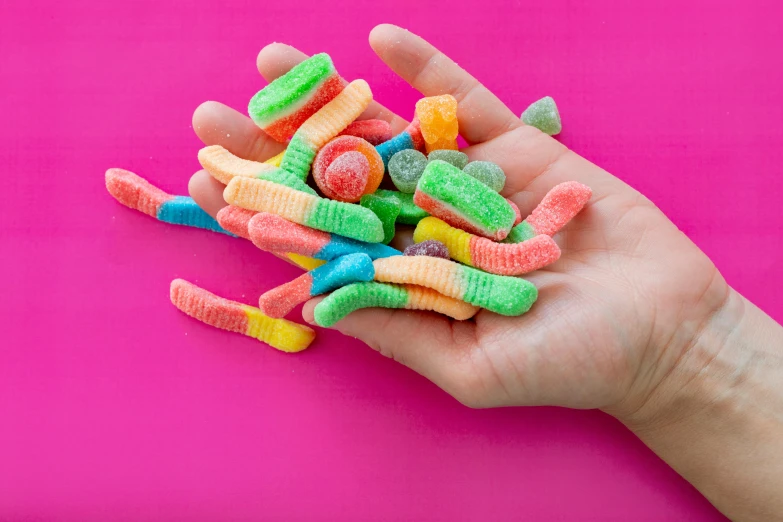 a hand holding a pile of gummy worms, by Rachel Reckitt, trending on pexels, a table full of candy, sherbert sky, seventies, jelly - like texture