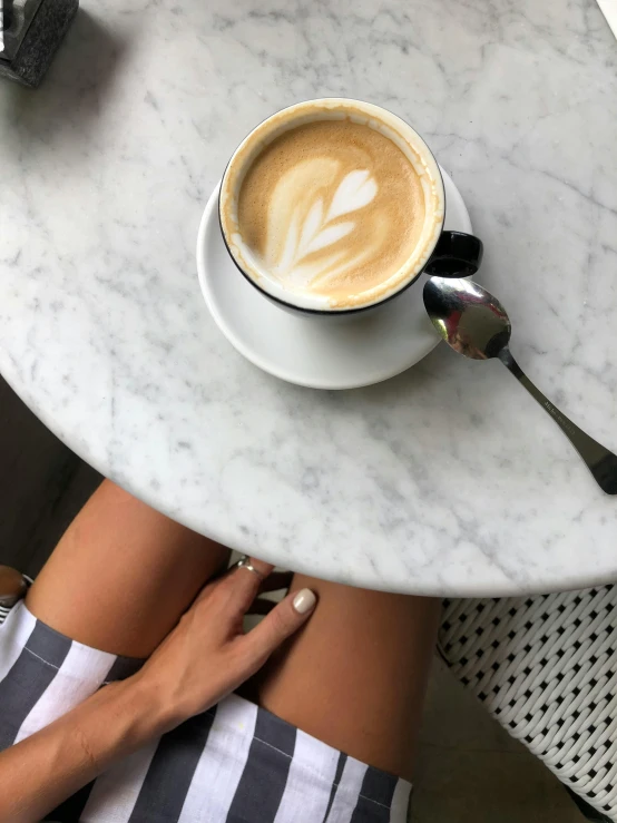 a woman sitting at a table with a cup of coffee, by Robbie Trevino, white miniskirt, instagram picture, all marble, victoria siemer