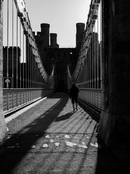 a black and white photo of a person walking across a bridge, a black and white photo, by John Gibson, caernarfon castle, high contrast!!, by greg rutkowski, high bridges