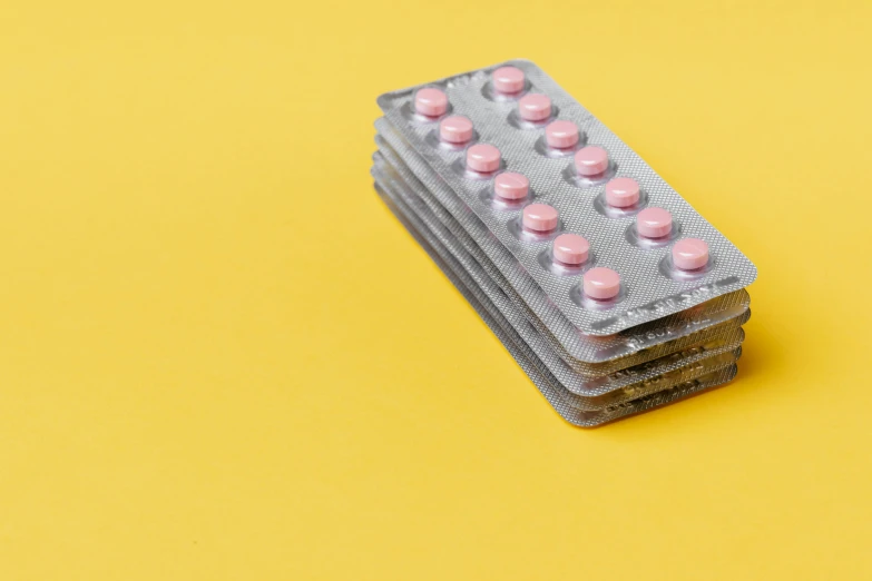 pills in a blister pack on a yellow background, by Rachel Reckitt, pexels, antipodeans, on grey background, pink, stacks, sitting on top a table