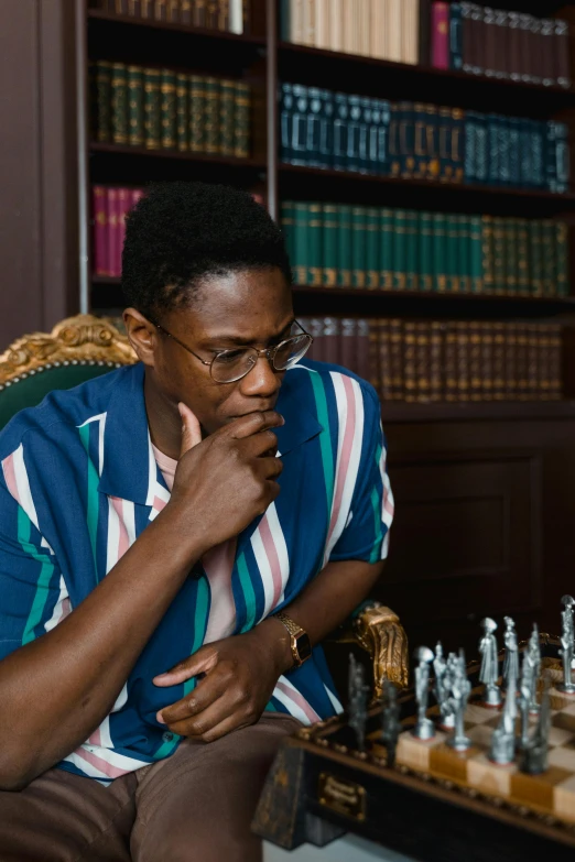 a man sitting in a chair playing a game of chess, an album cover, inspired by Barthélemy Menn, trending on unsplash, kehinde wiley, man with glasses, thumbnail, ( ( theatrical ) )