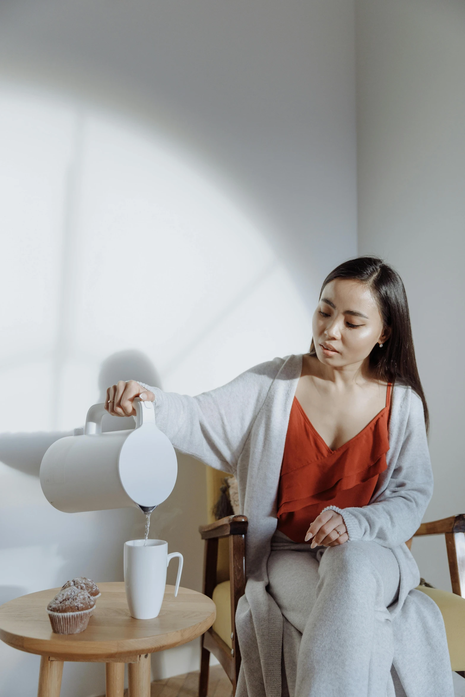 a woman sitting in a chair pouring something into a cup, by helen huang, pexels contest winner, minimalism, wearing a light shirt, concerned, kettle, gif