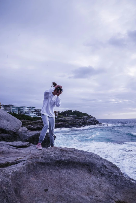 a man standing on top of a rock next to the ocean, an album cover, inspired by Sydney Carline, unsplash, happening, dabbing, harsh flash photo, street photo, drinking