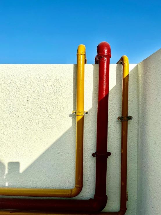 a red fire hydrant sitting next to a white wall, an abstract sculpture, by Doug Ohlson, guardrails, shades of yellow, seaside, heavy conduits