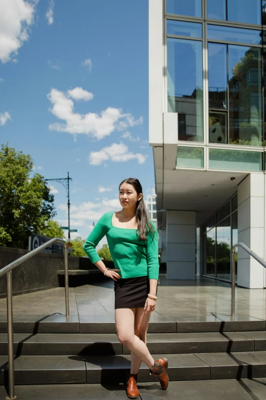 a woman standing on some steps in front of a building, gemma chen, green square, posed, student