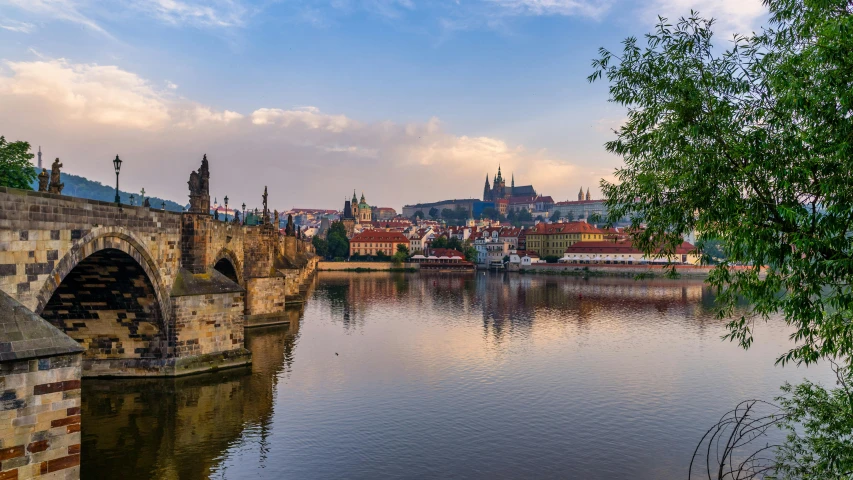 a bridge over a river with buildings in the background, by Tom Wänerstrand, pexels contest winner, art nouveau, prague in the background, slide show, panoramic shot, lakeside