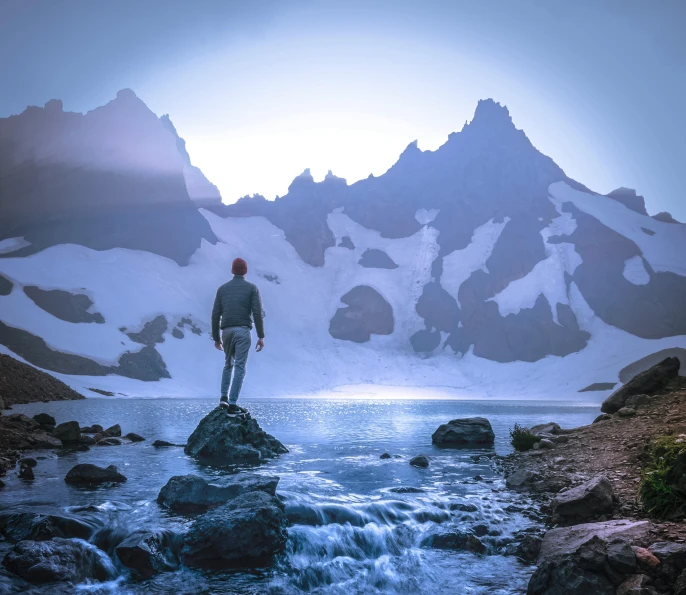 a man standing on top of a rock next to a body of water, a matte painting, pexels contest winner, majestic snowy mountains, backlite, mountain lakes, trending on