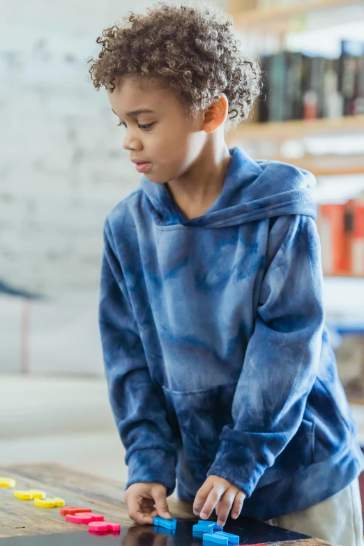 a young boy playing with blocks on a table, inspired by George Henry, trending on unsplash, hoodie, tie-dye, wearing blue, detail shot