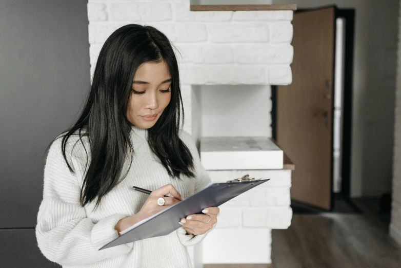 a woman in a white sweater writing on a clipboard, pexels contest winner, gemma chan, grey, low quality photo, background image