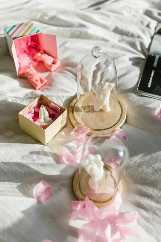 a couple of figurines sitting on top of a bed, a marble sculpture, by Eden Box, unsplash, romanticism, dreamscape in a jar, packaging, on a wooden tray, pink