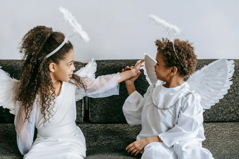 two little girls dressed as angels sitting on a couch, pexels contest winner, hurufiyya, feather hair ornaments, joseph and joseph, reaching out to each other, white and black clothing