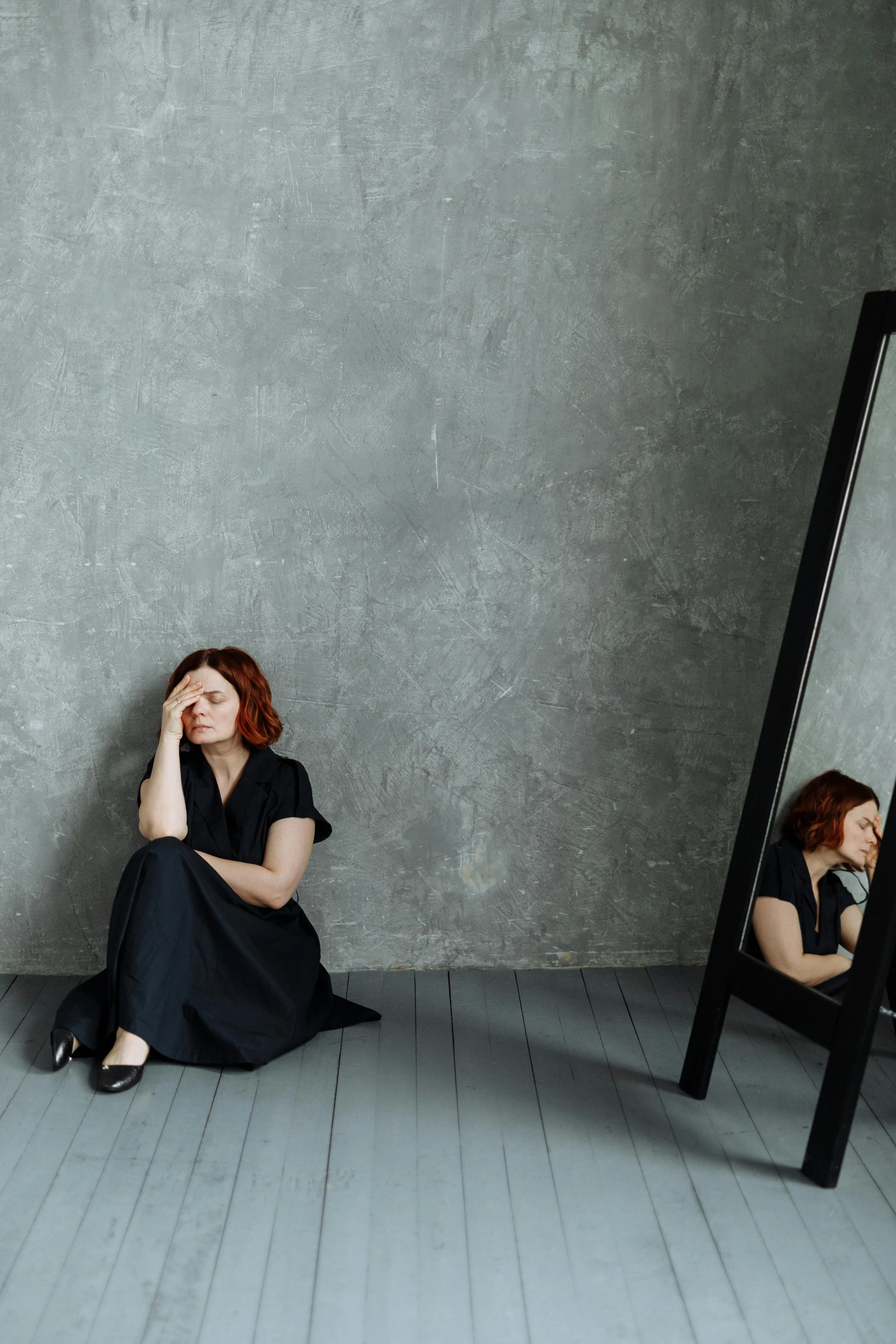 a woman sitting on the floor in front of a mirror, inspired by Anna Füssli, trending on pexels, renaissance, sad christina hendricks, on a gray background, wearing a black dress, fullbody or portrait