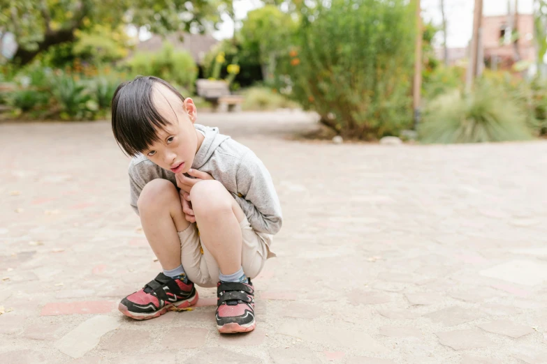 a little boy sitting on top of a skateboard, by Winona Nelson, unsplash, visual art, young cute wan asian face, pouting, in garden, they are crouching