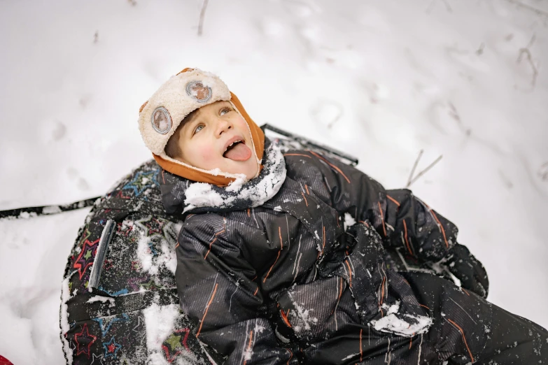 a young boy laying in the snow on skis, a portrait, by Emma Andijewska, pexels contest winner, process art, excited, thumbnail, black, brown