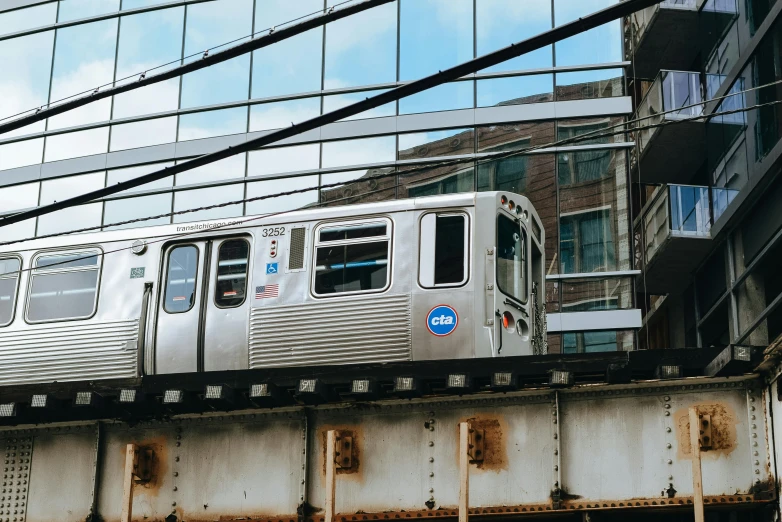 a silver train traveling over a bridge next to a tall building, by Carey Morris, unsplash, graffiti, chicago, monorail, brown, window