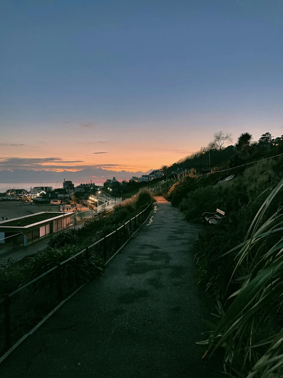 a bench sitting on the side of a road next to a body of water, cliff side at dusk, wellington, walking through a suburb, slide show