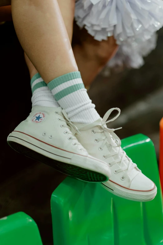 a person sitting on top of a green bench, wearing white sneakers, striped socks, converse, sitting on a store shelf